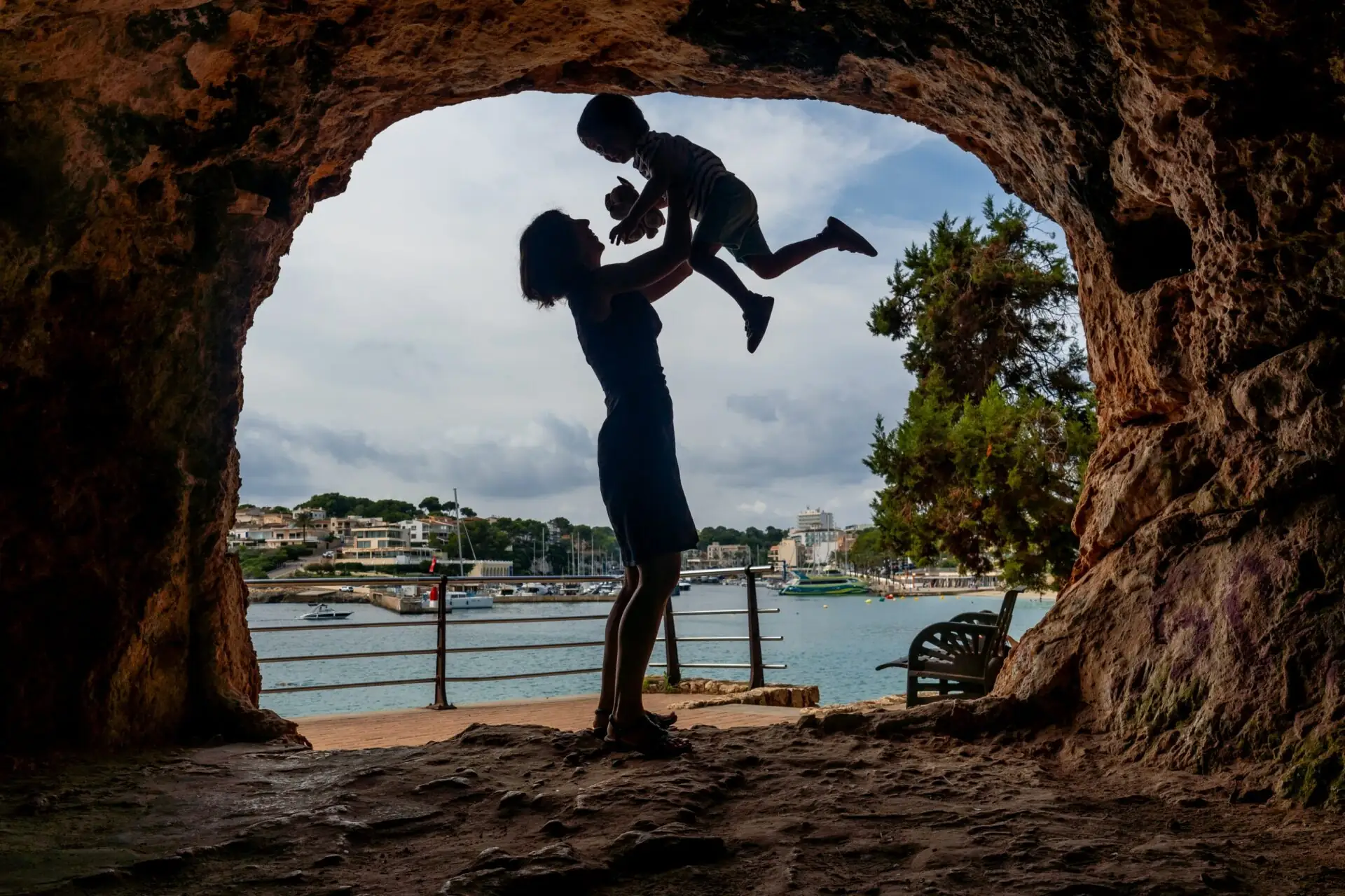 Mutter hebt Sohn in einer Höhle mit Blick auf den Hafen von Puerto Cristo auf Mallorca