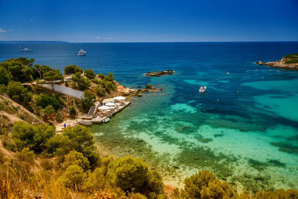Eine ruhige Aufnahme des Strandes von Portals Nous (Playa Oratorio) auf Mallorca, wo goldener Sand auf klares blaues Wasser trifft.