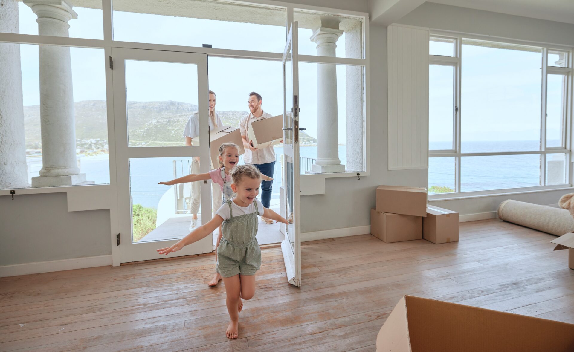 Familie bezieht ein Haus am Meer in Andratx, Kinder spielen Flugzeug, Eltern betreten mit Kosten das Haus - alle Lachen.
